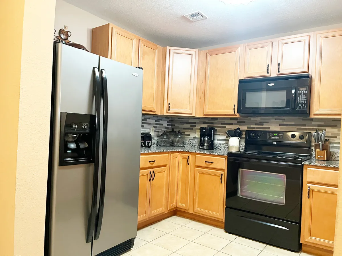 A well-appointed kitchen with stainless steel refrigerator, black oven, granite countertops, and warm wooden cabinetry. The space is designed for cooking, entertaining, and preparing everything from holiday feasts to midnight snacks.