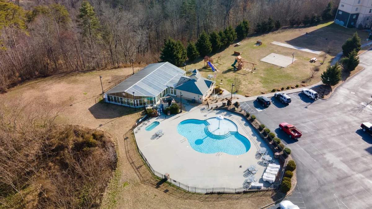 This vibrant exterior shot captures the resort’s outdoor swimming pool area, complete with colorful playground equipment, a clubhouse, and ample lounging areas. Children are seen laughing and playing while families gather nearby, giving a sense of lively community and fun.