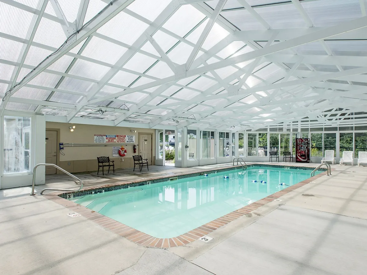 Bright natural light pours through the glass roof of the spacious indoor pool, where guests enjoy relaxing swims on comfortable lounge chairs. The area is clean, modern, and climate-controlled, ideal for year-round aquatic fun.