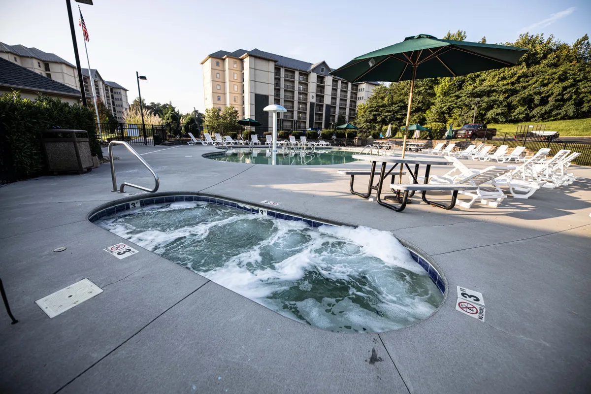 The image showcases a sparkling swimming pool and inviting hot tub surrounded by lounge chairs, an umbrella, and a picnic table. The setting captures a tranquil outdoor environment where groups can relax, socialize, and enjoy the resort amenities together.