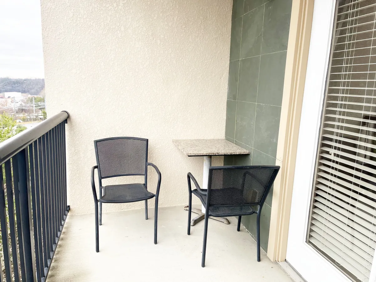 A cozy exterior patio scene featuring two black chairs and a small table against a green tiled wall. The setup is inviting for morning coffee, reading, or enjoying fresh air, offering a tangible outdoor experience for guests.