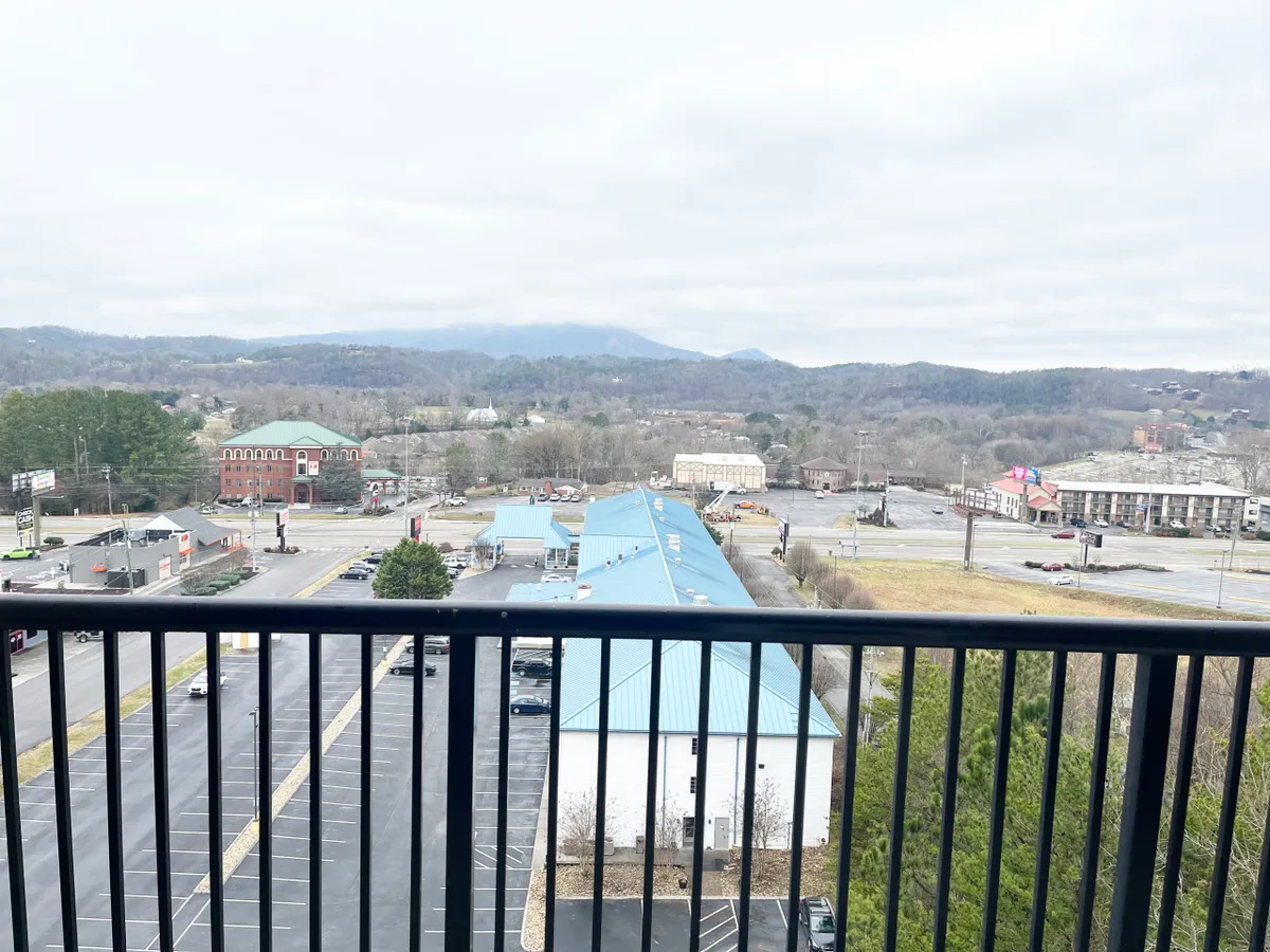 A view from the condo balcony that encompasses the surrounding area, featuring mountains in the background, commercial buildings, and a visible parking lot. This scene offers a real sense of the property's location and its easy access to local attractions and amenities.