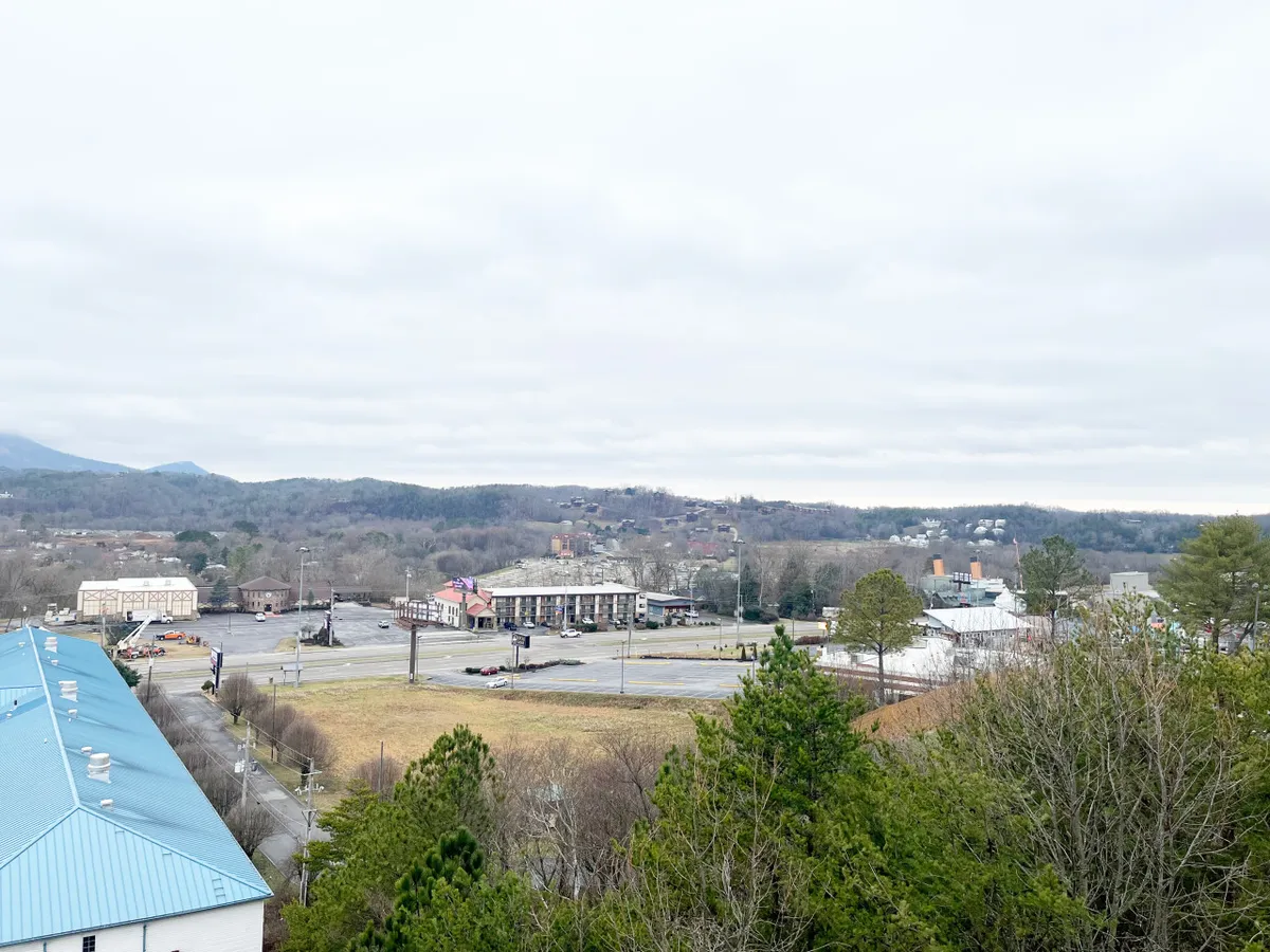 A scenic view of mountains rising beyond commercial buildings, with greenery in the foreground and an empty parking lot. The image evokes the sense of adventure and exploration available just outside the condo, highlighting proximity to local attractions and the area's natural beauty.