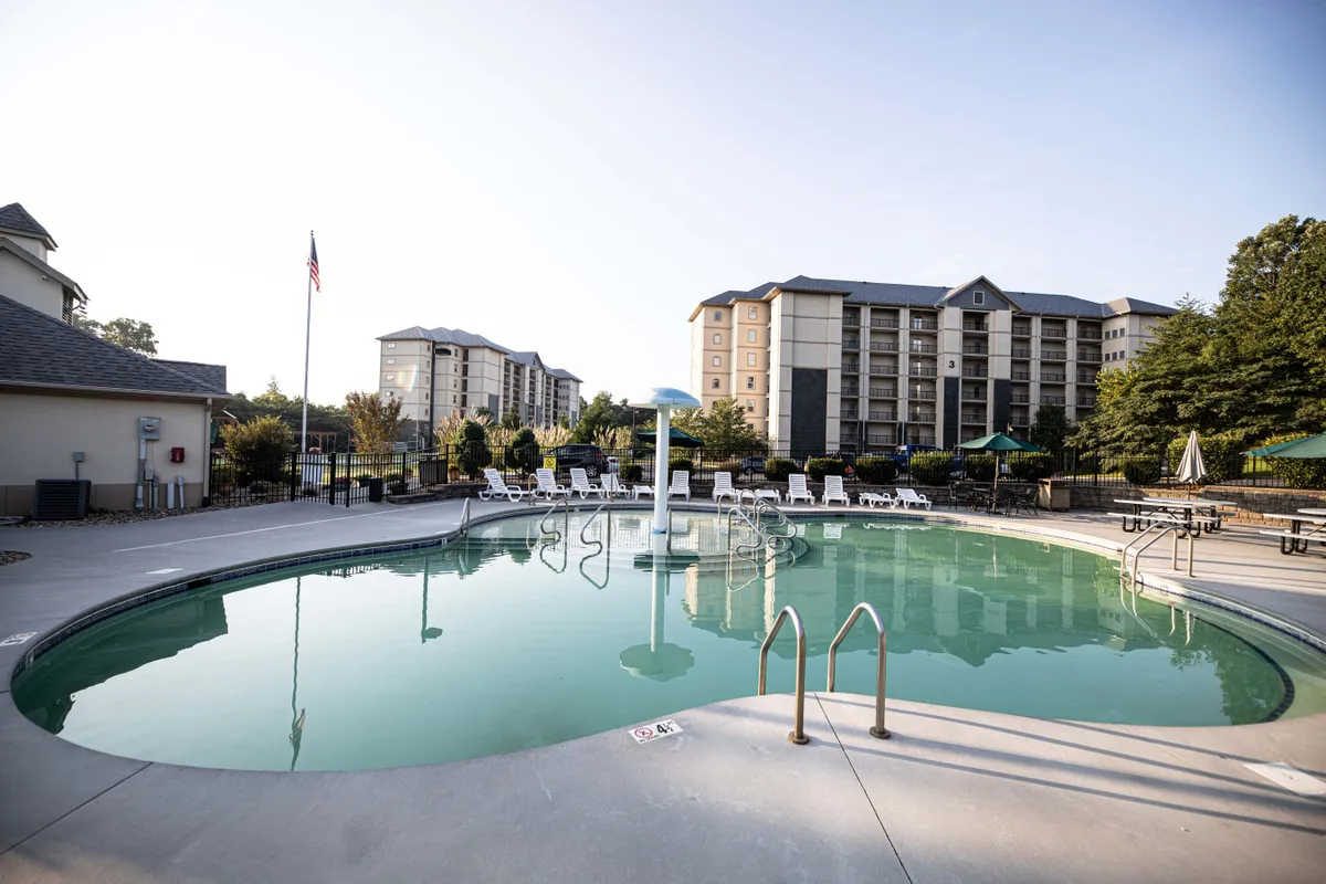 This image shows a sparkling outdoor swimming pool surrounded by lounge chairs, set amidst lush greenery with buildings in the background. The scene is sunlit and inviting, suggesting a welcoming atmosphere for families to relax, play, and enjoy quality time together outdoors.